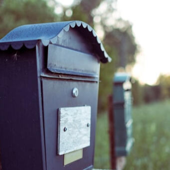 black mailbox in the country with faded grass and trees in the background